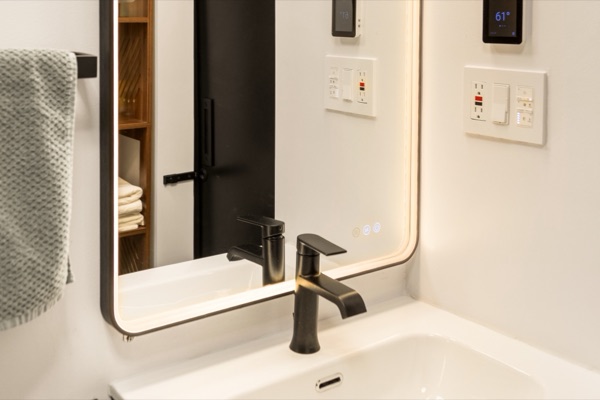 A backlit mirror over a white sink with a matte black faucet