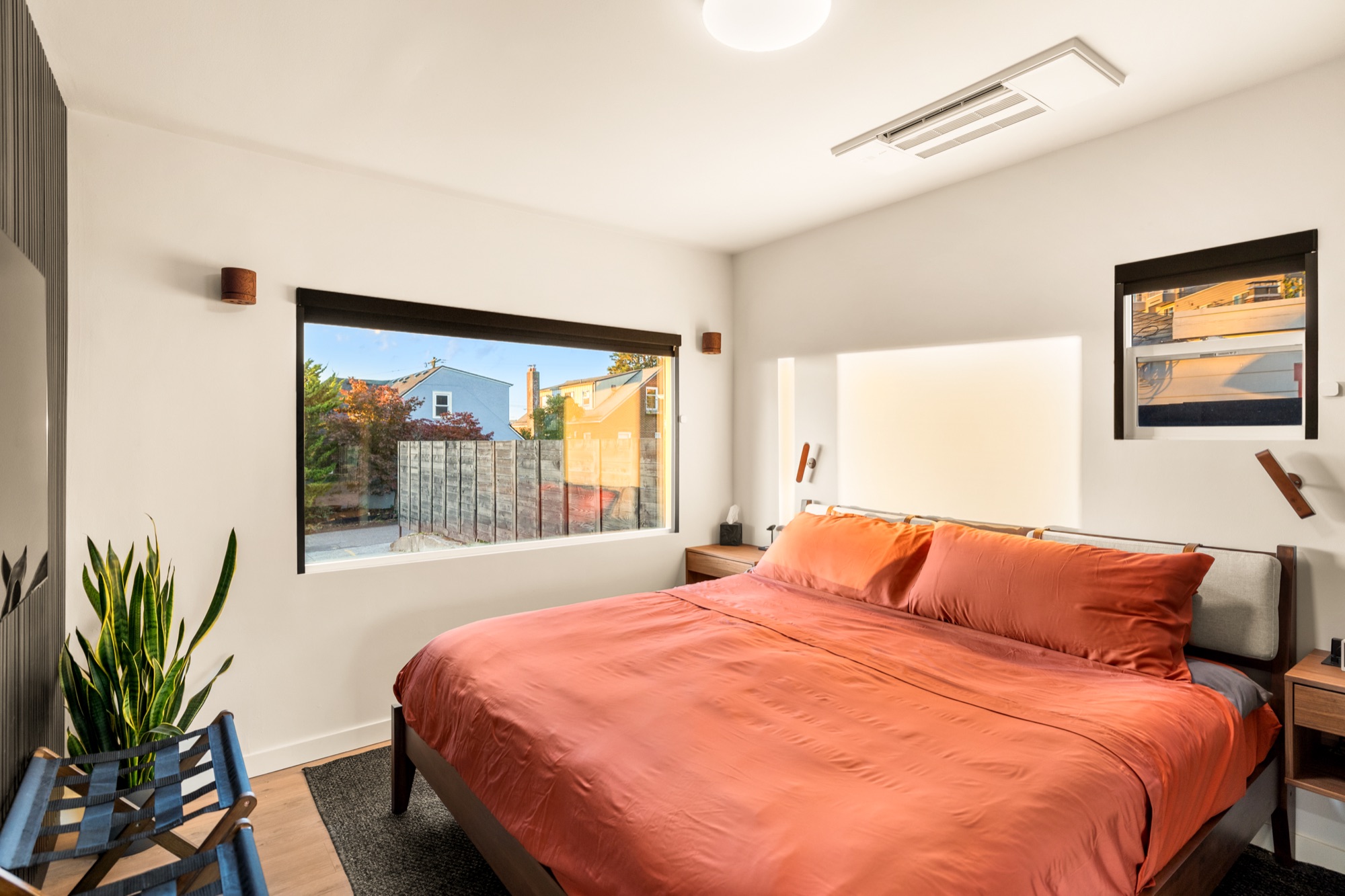 King bed in rust-colored linens with an upholstered headboard and wood nightstands, beside a large picture window
