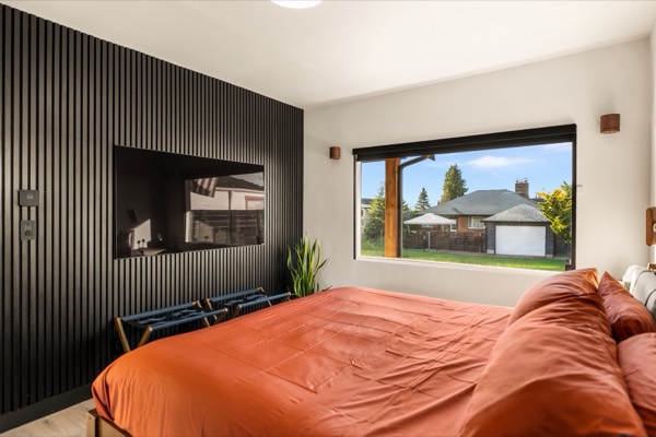 Primary bedroom with a king bed in rust-colored linens, a black slatted feature wall with a TV and a large picture window