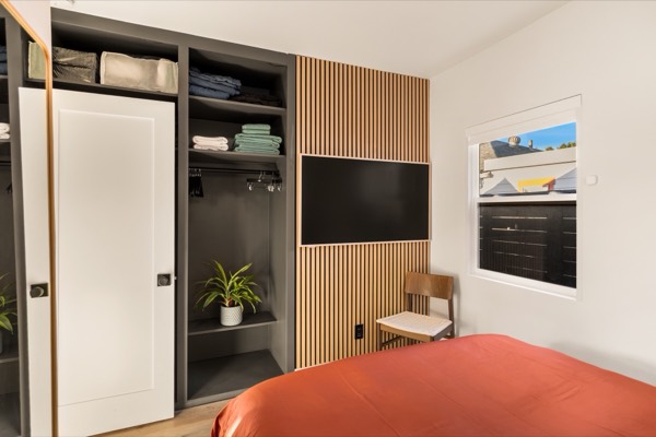 Second bedroom with a closet of open shelves and folded linens, and a TV on a light wood slat wall