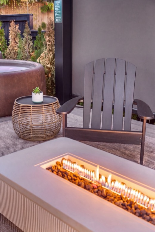 The gas fire pit lit at dusk beside an Adirondack chair, with the Softub and evergreens behind