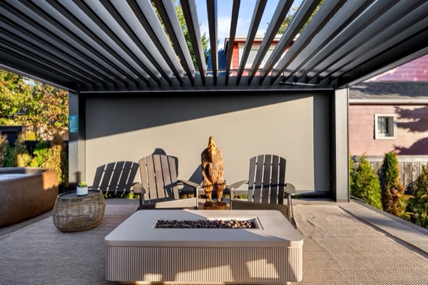 A gas fire pit, two Adirondack chairs and a carved wooden bear under the louvered pergola, with the edge of the Softub at left