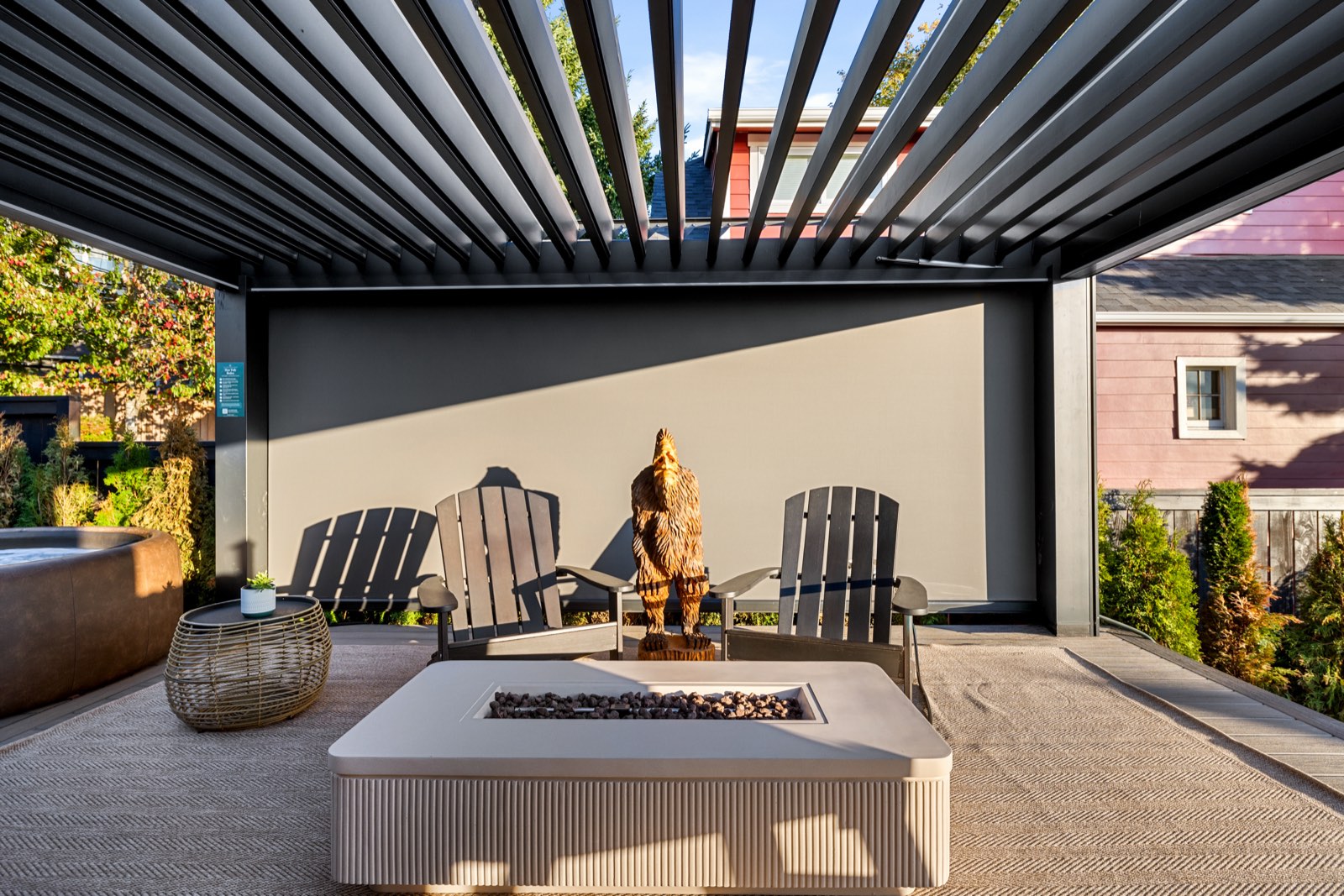 Under the louvered pergola on the back deck: a gas fire pit, two Adirondack chairs and a carved wooden bear, with the edge of the Softub at left.
