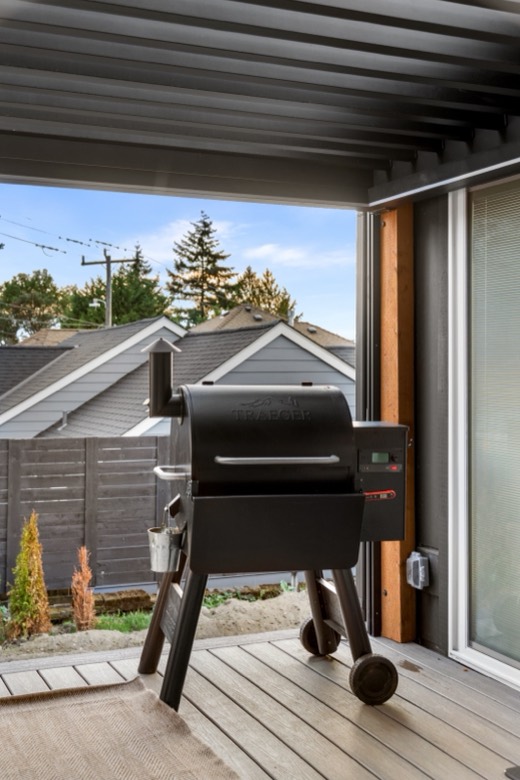 A grill on the back deck under the pergola, with neighboring rooftops beyond the fence