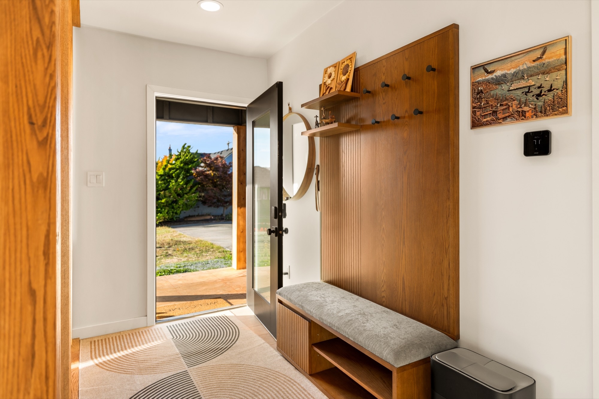 The entry: the front door open to the porch, beside a slatted wood coat wall and a bench.