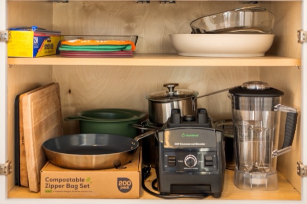 An open kitchen cabinet with cutting boards, a Dutch oven, pans, a pot and a blender