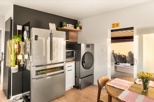 A stainless French-door fridge beside an all-in-one washer-dryer, with the dining table in the foreground