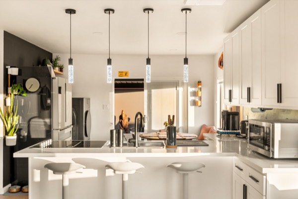 Kitchen island with bar stools under pendant lights, with sunlight across the white counters