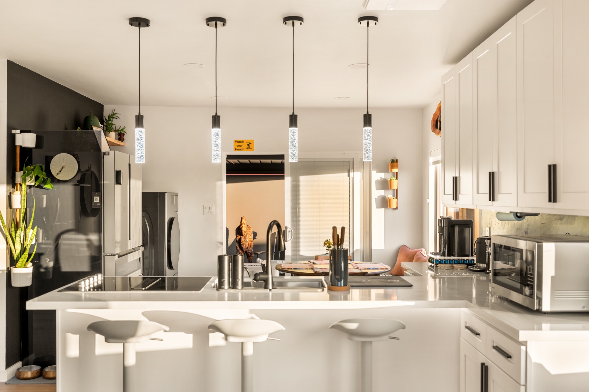 The kitchen in golden light: white cabinets and counters, pendant lights and stools at the island.