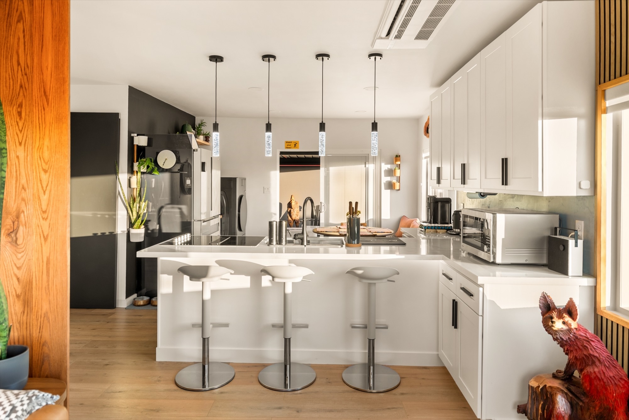 Bright white kitchen with pendant lights over island seating, an induction cooktop and a carved wooden fox by the counter.