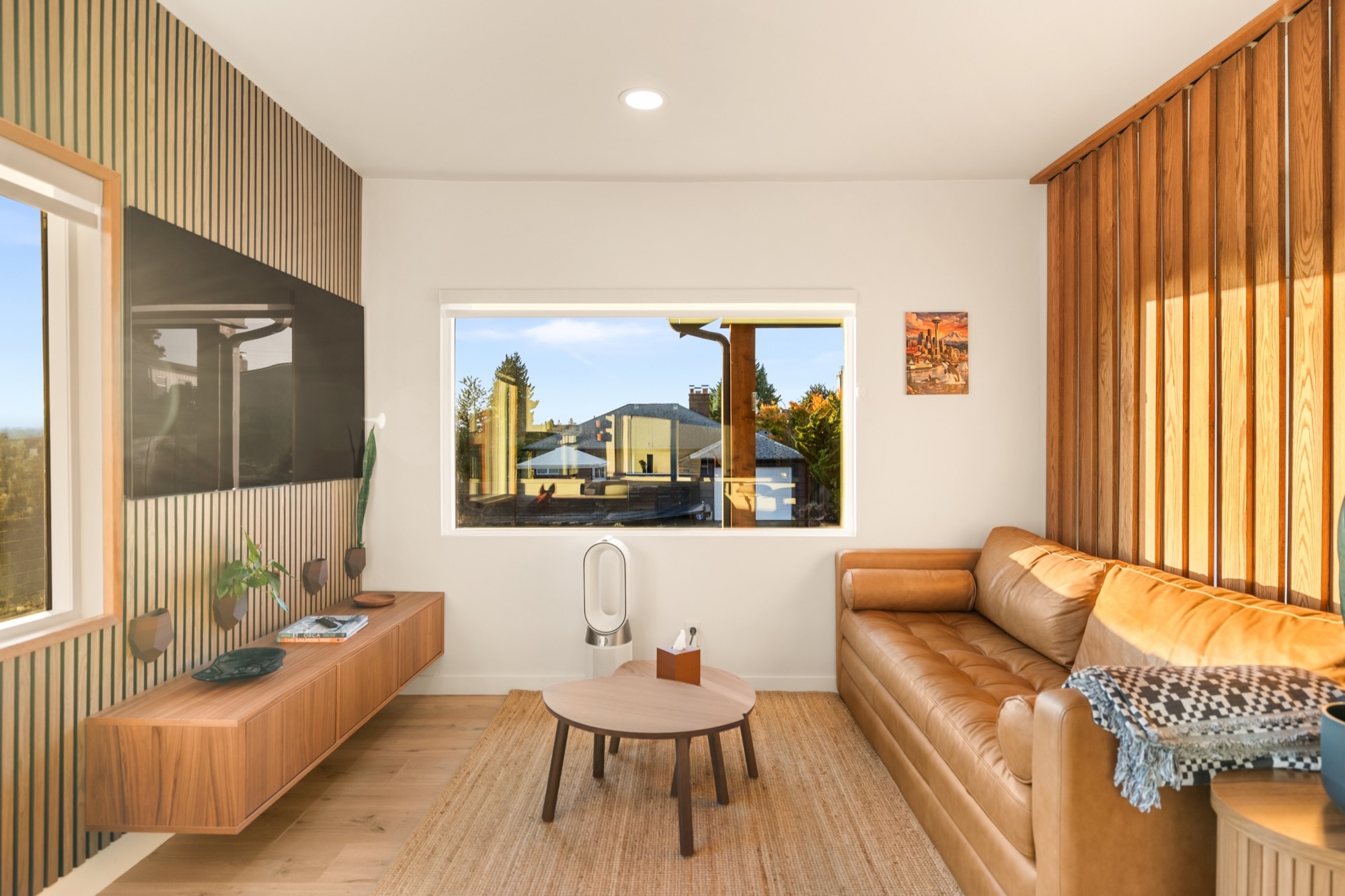 Living room with a tan leather sofa, wood slat walls and a picture window.